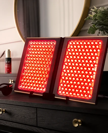 Panneau FOREO FAQ™ Dual LED Panel diffusant une lumière rouge sur une coiffeuse, à côté du sérum FAQ™ Red Light Peptide et des lunettes de protection.